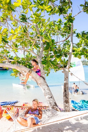 A beach scene with a hammock, a sailboat, and people relaxing under trees. - Holiday Inn Resort Vanuatu by IHG (Port Vila)