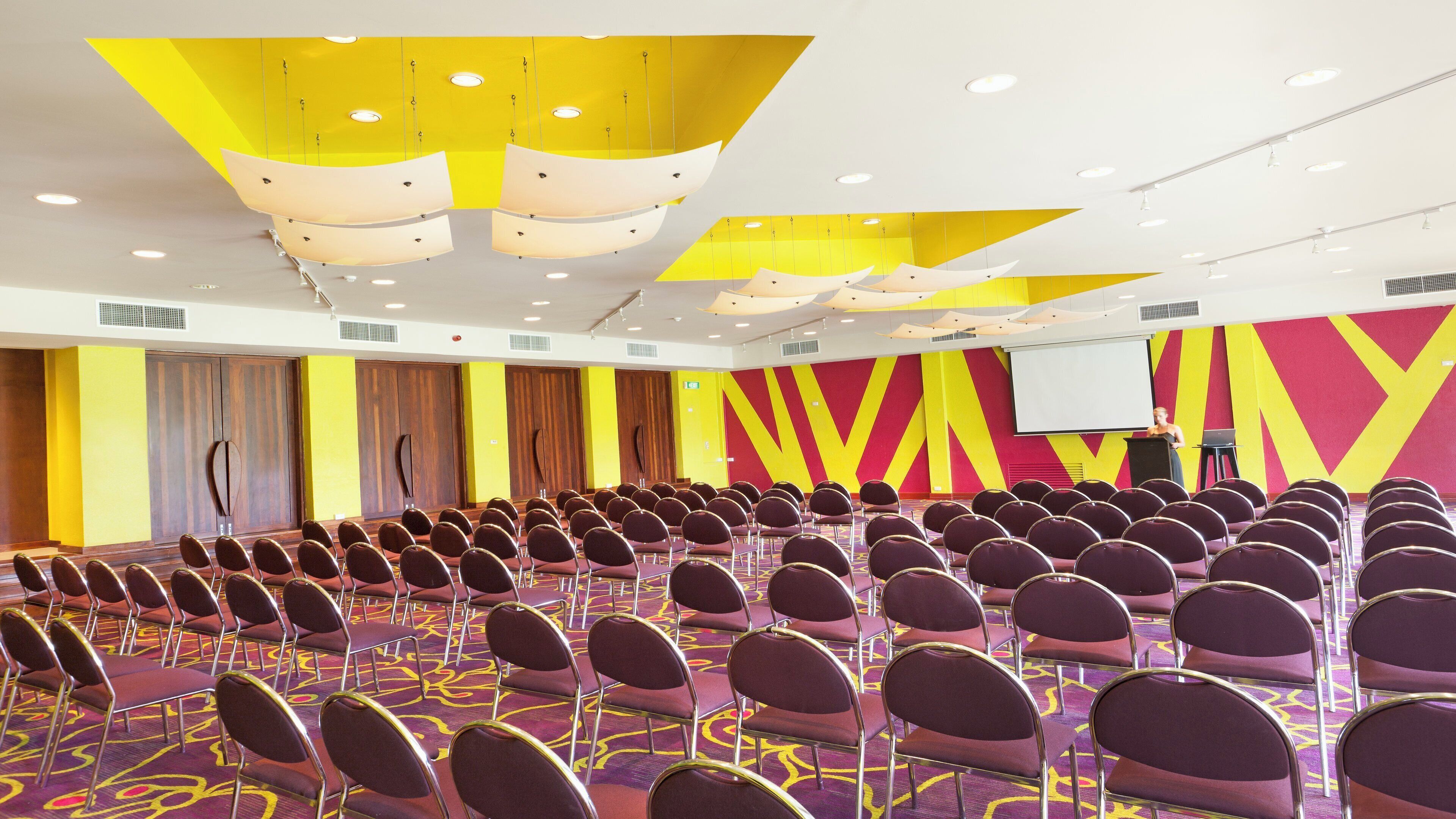 A conference room with rows of chairs, a podium, and a screen.
