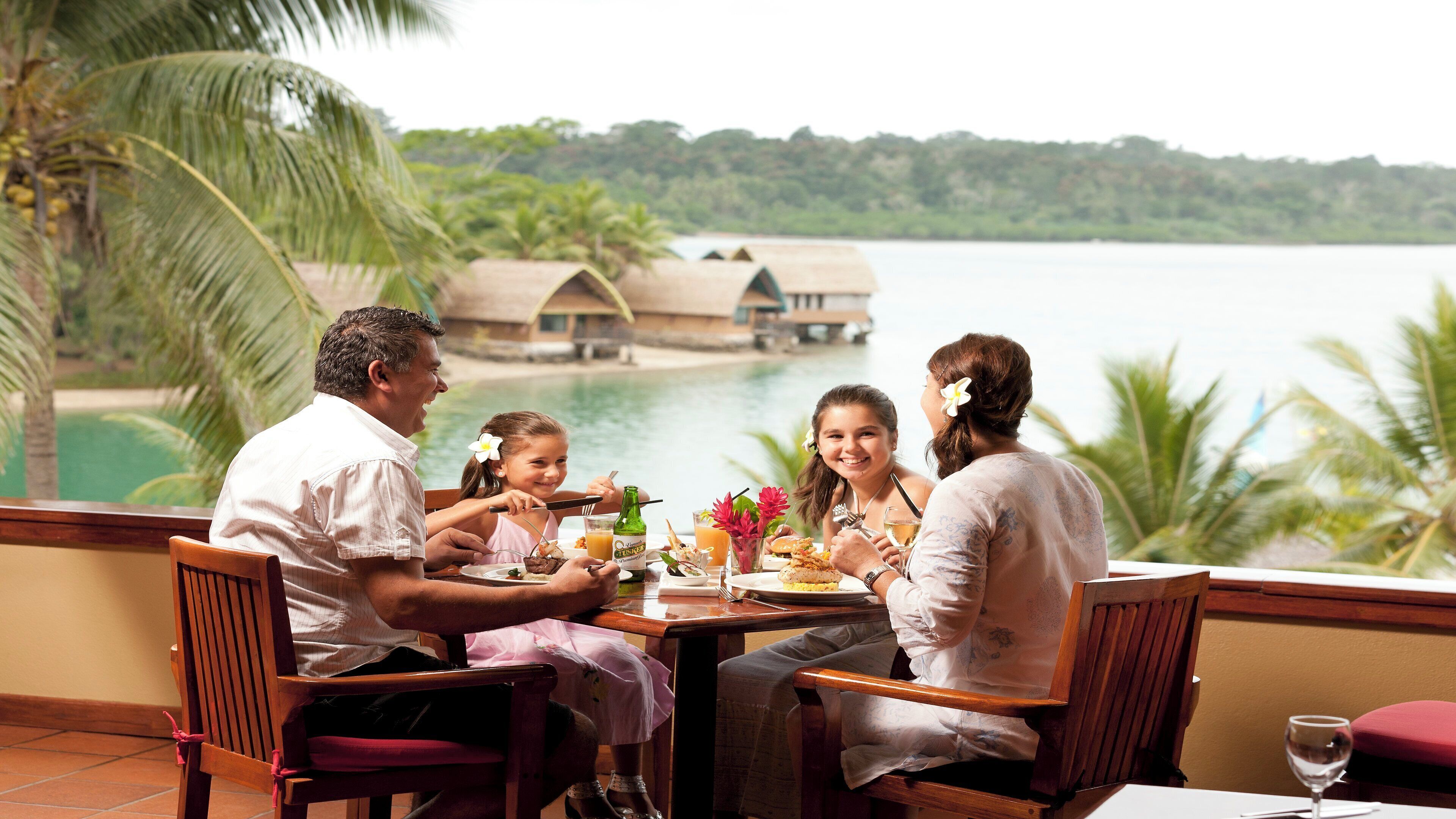 A dining table with a view of a lake and overwater bungalows.