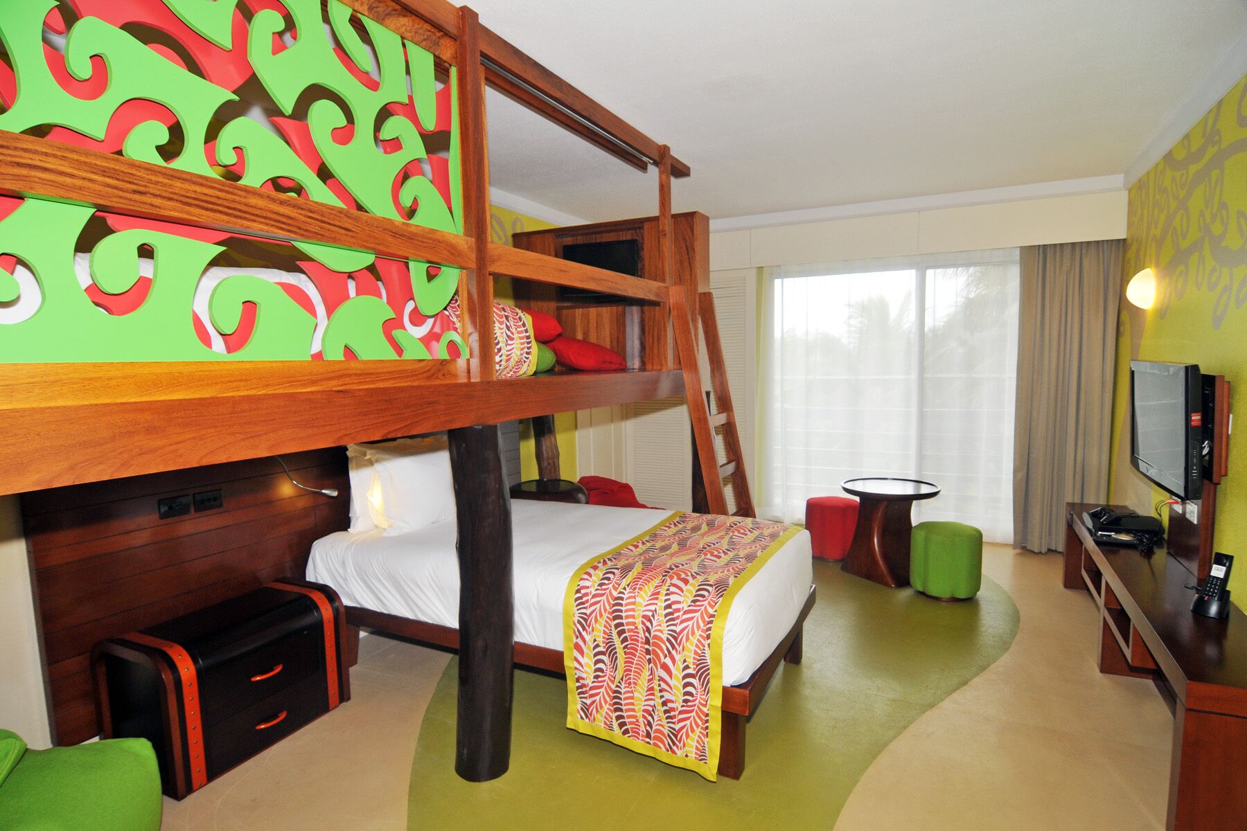 Une chambre d’hôtel avec un lit superposé, un bureau avec un ordinateur, une télévision et une grande fenêtre avec des rideaux.