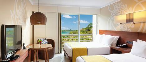 Habitación de hotel con cama, televisión, escritorio, silla y balcón con vista al océano.