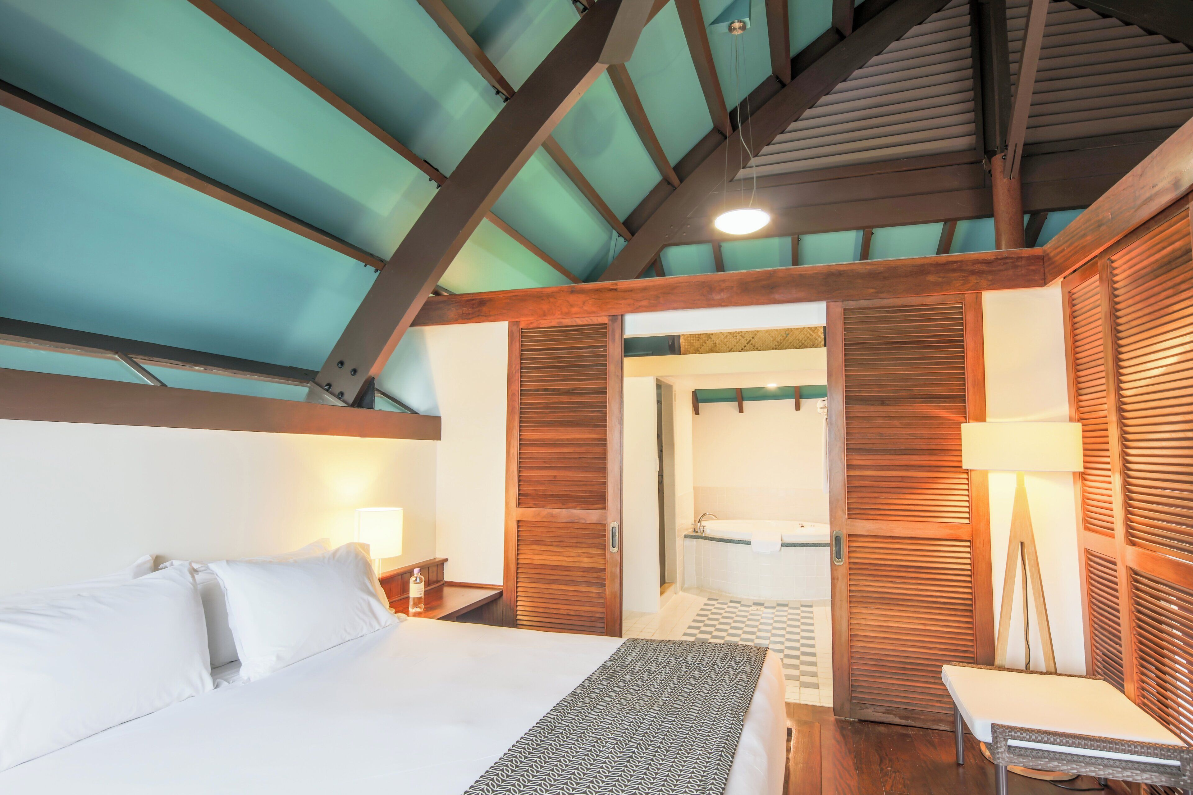 A hotel room with a bed, bedside table, lamp, and a view of the bathroom.