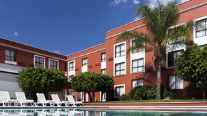 A modern building with a swimming pool, white lounge chairs, and palm trees. - Fiesta Inn Leon (León)