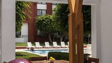 Un área de estar al aire libre con vista a la piscina, mesas y sillas de madera.