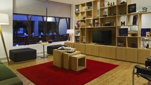 A modern living room with a large window, a red rug, a TV, and a bookshelf. - Fiesta Inn Leon (León)