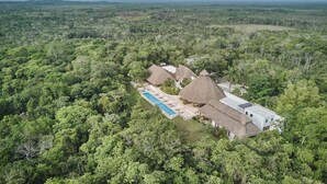 An aerial view of a resort with thatched-roof buildings, a swimming pool, and dense forest surroundings. - The Explorean Selva Maya Kohunlich (Kohunlich)