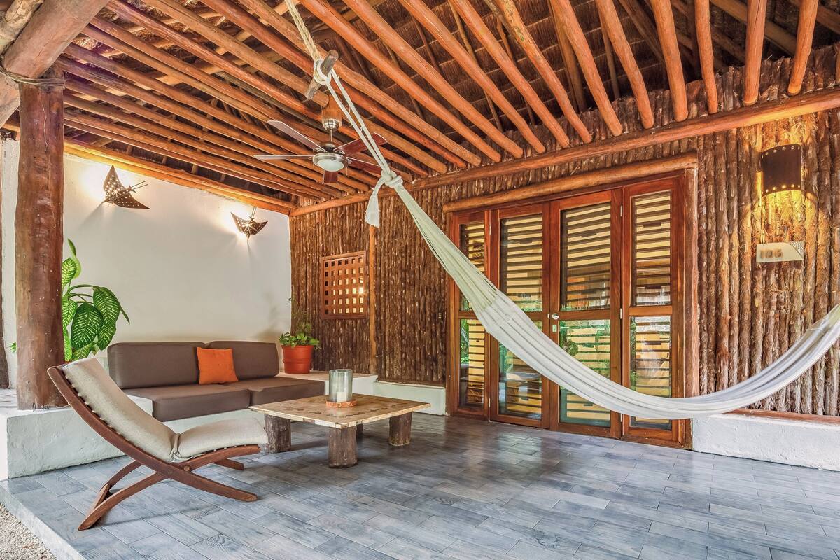 A cozy room with a hammock, wooden ceiling, and a sofa with cushions.