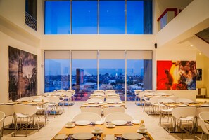 A dining area with tables set for service, large windows offering a city view, and artwork on the walls. - Fiesta Inn Tlalnepantla (Tlalnepantla de Baz)