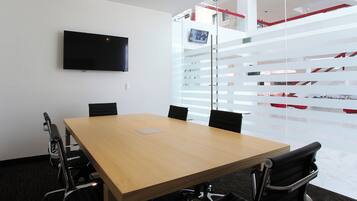 Un salón de conferencias con una gran mesa, cuatro sillas, un televisor de pantalla plana y un panel de vidrio con detalles rojos.
