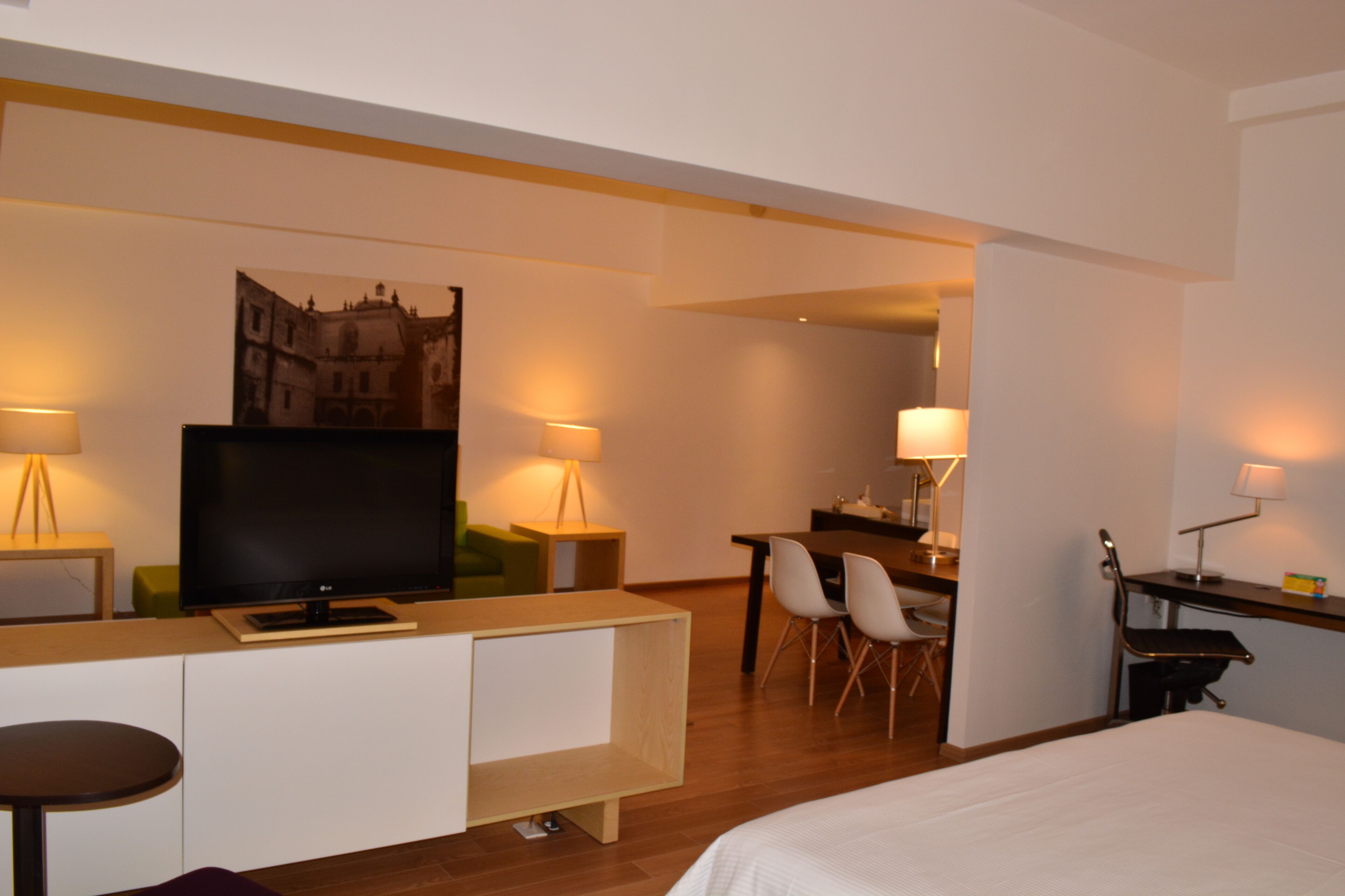 A hotel room with a bed, a desk with a chair, a television, and two lamps.