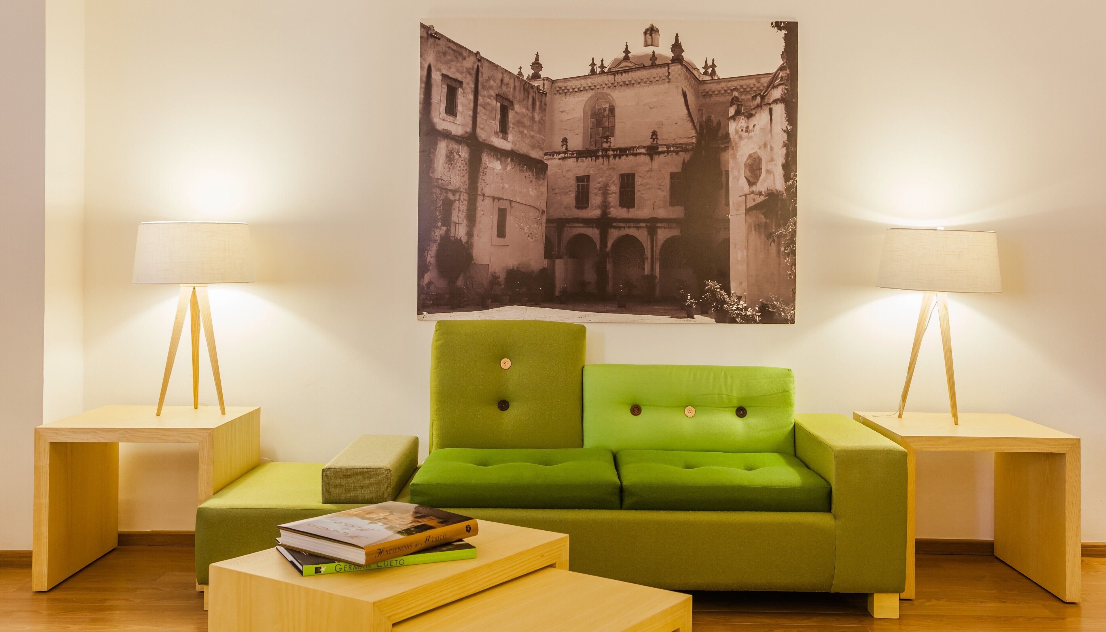 A room with a green sofa, two bedside tables with lamps, a wooden coffee table, and a framed picture on the wall.