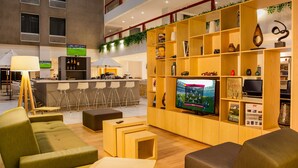 Eine moderne Hotelhalle mit Barbereich, Sitzgelegenheiten und einem großen Fernseher.