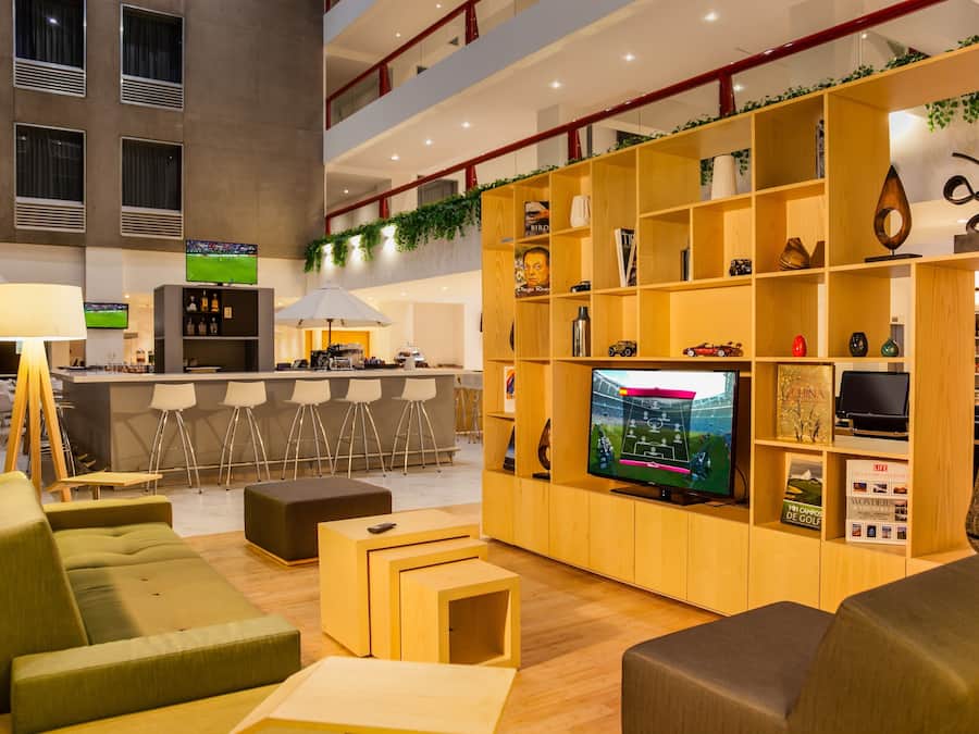 A modern hotel lobby with a bar area, seating, and a large TV screen.