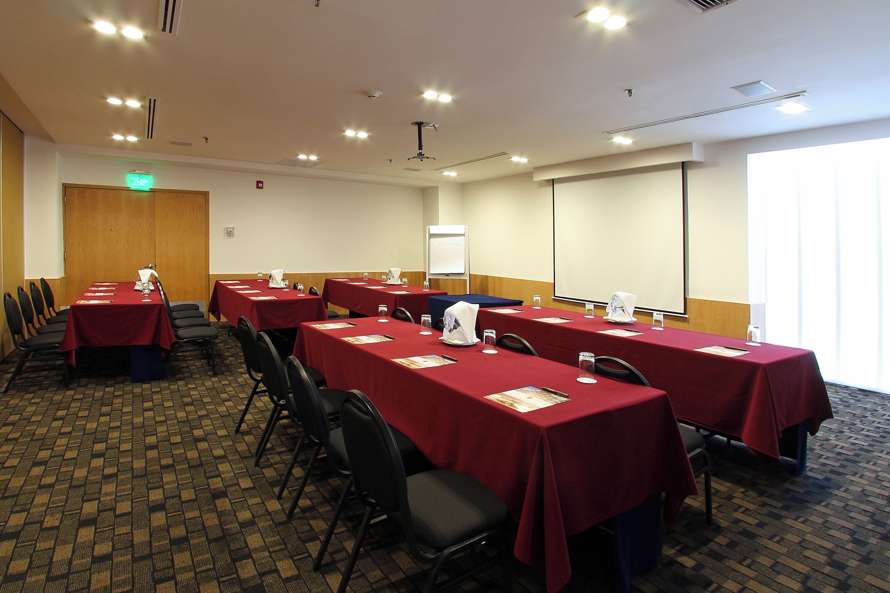 Une salle de conférence avec plusieurs tables recouvertes de nappes rouges, disposées en rangées et entourées de chaises.