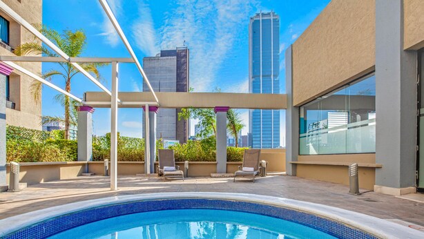 A rooftop pool with a clear view of the city skyline, surrounded by lounge chairs and palm trees. - CHN Hotel Monterrey Centro, Trademark by Wyndham (Monterrey)