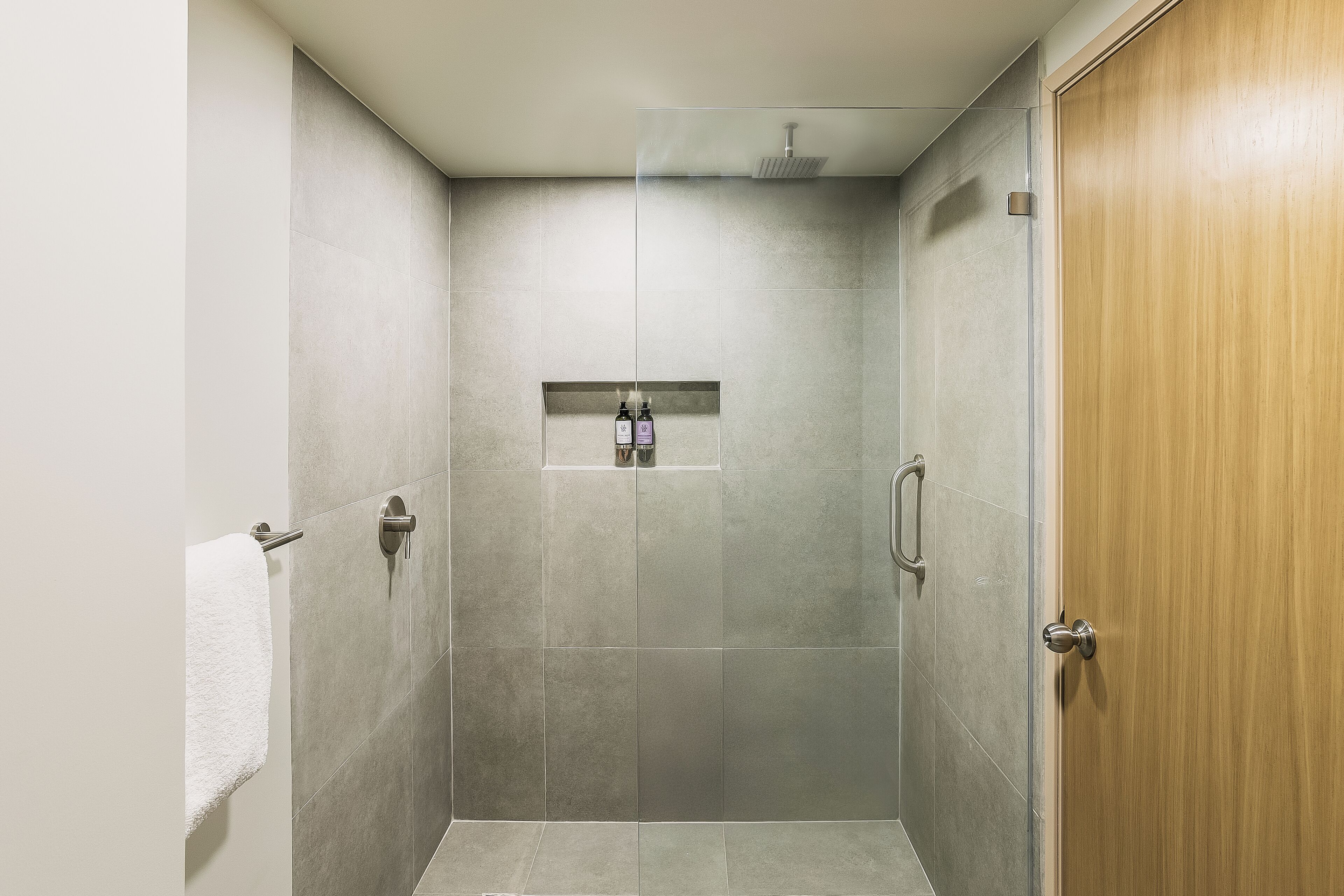 Een douche met glazen deur, een handdoekhouder en een houten deur.