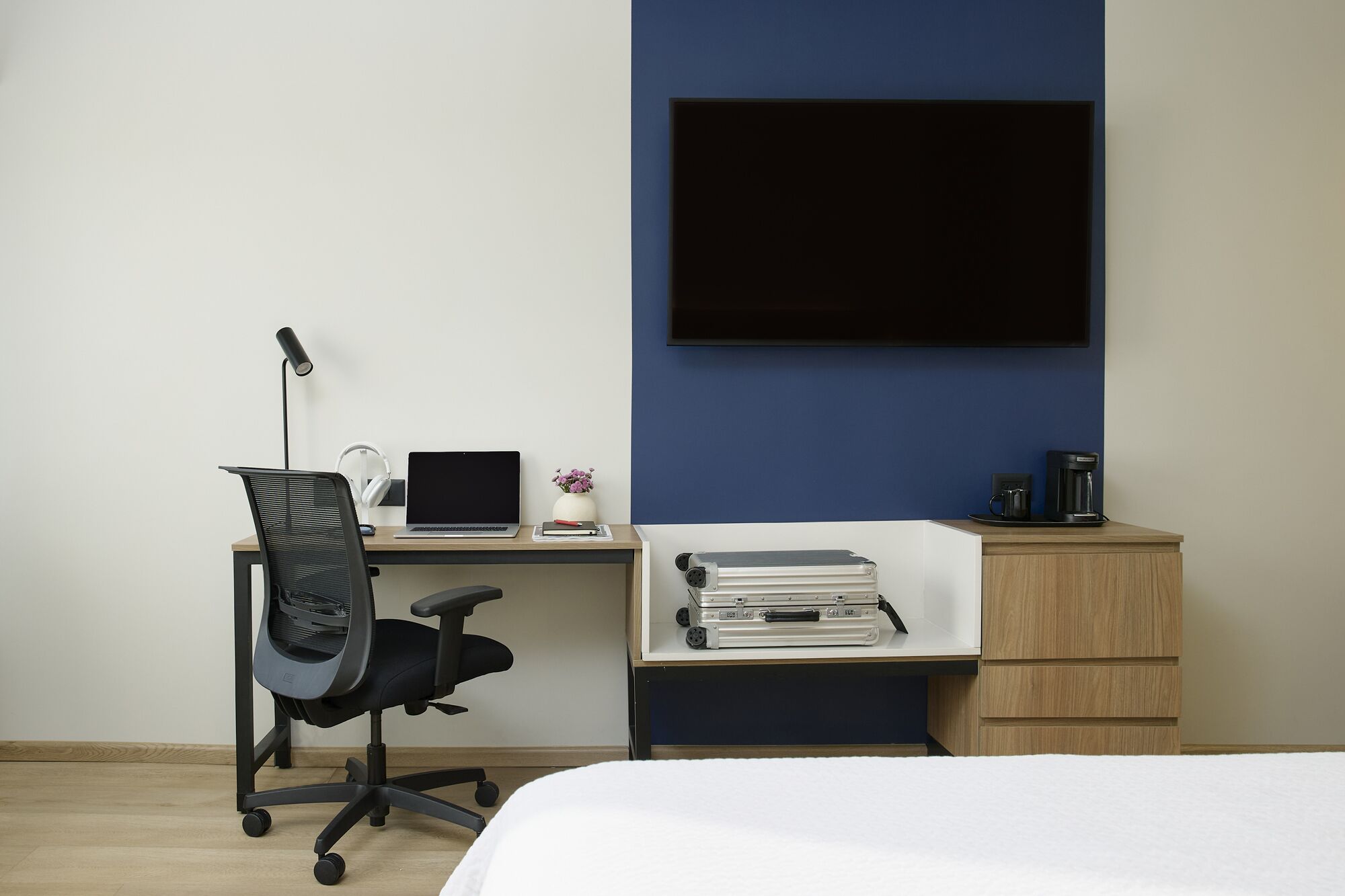 A neatly organized bedroom with a bed, a desk with a laptop, headphones, and a small plant.