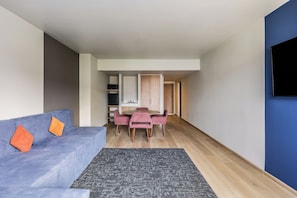 A modern living room with a sofa, a dining table with chairs, and a flat-screen TV mounted on the wall. - Fiesta Inn Monterrey La Fe (San Nicolas de los Garza)