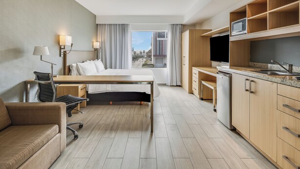 Ett hotellrum med en säng, skrivbord, stol, ett litet kök och utsikt över staden.