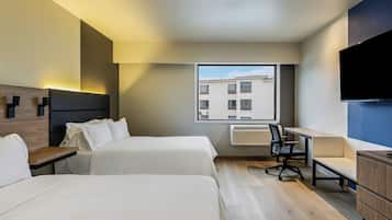 A hotel room with two beds, a desk, a chair, a TV, and a window with a view of buildings.