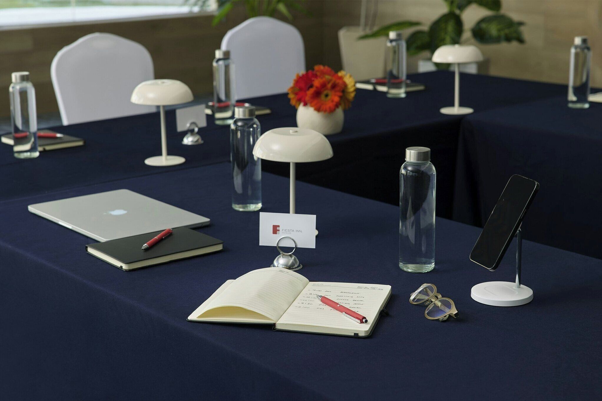 Une table de conférence avec un ordinateur portable, un bloc-notes, un stylo, des lunettes et une bouteille d’eau.
