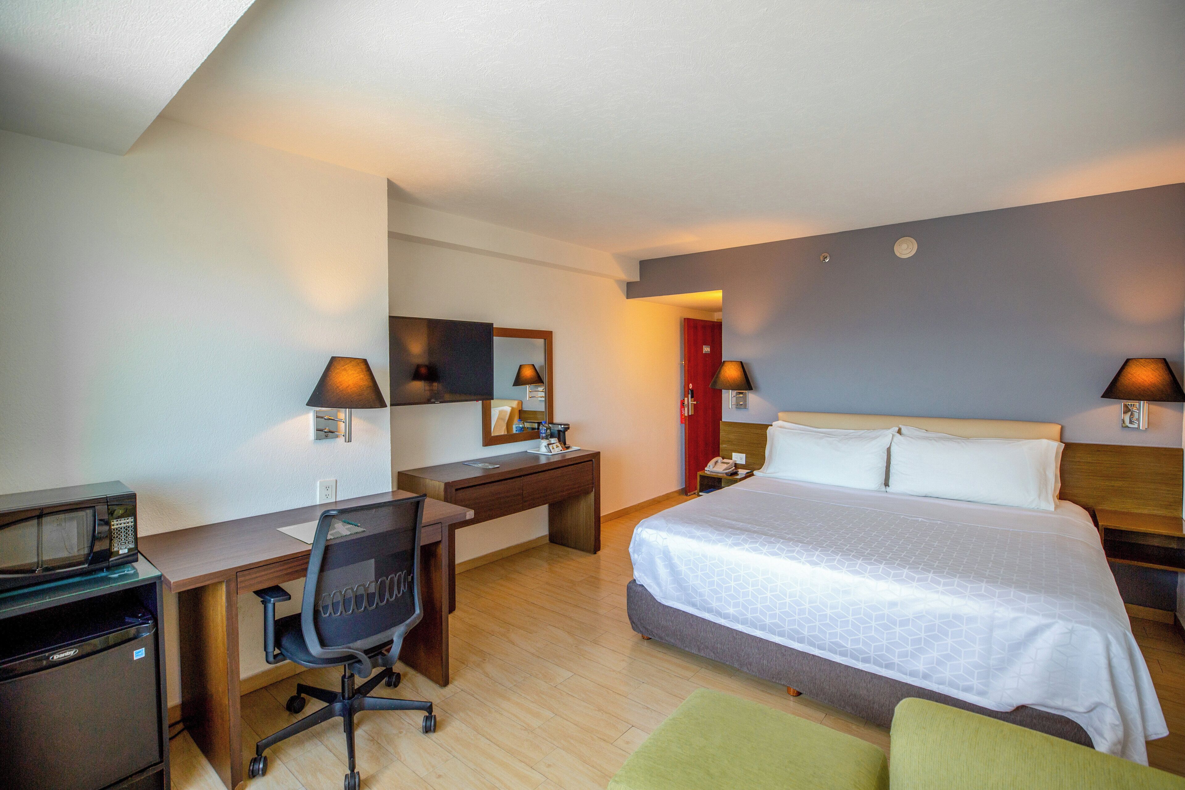 A hotel room with a bed, desk, chair, and a microwave.