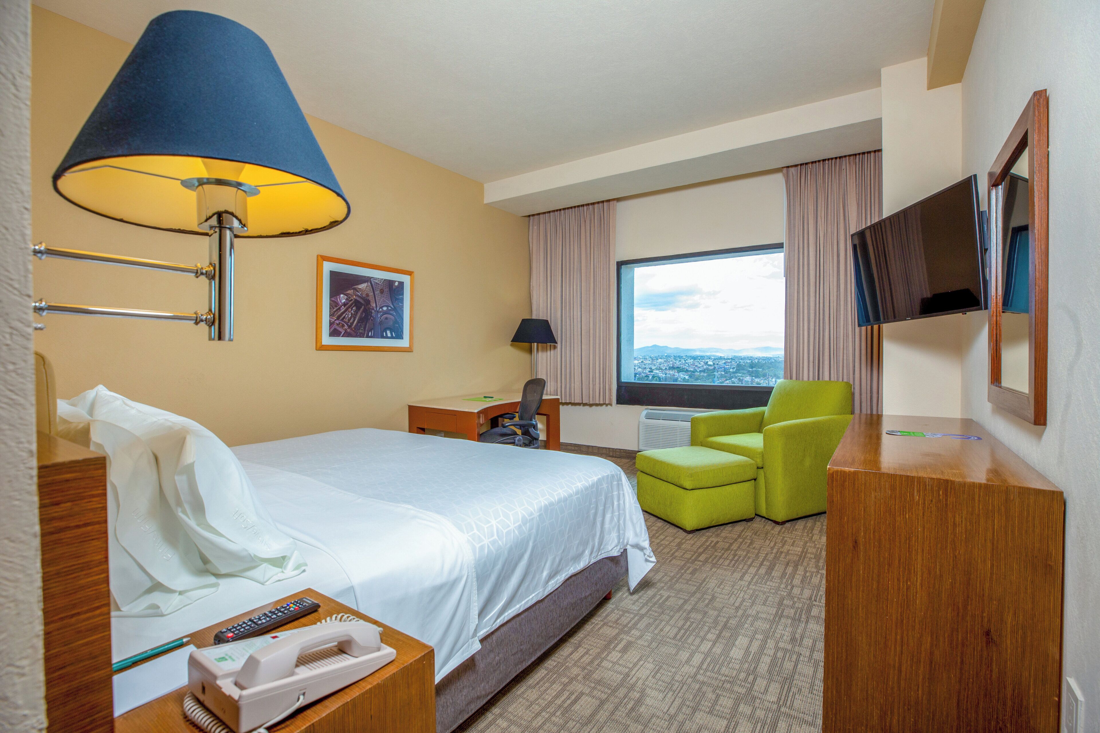 A hotel room with a bed, a desk, a chair, a TV, and a window with a view.
