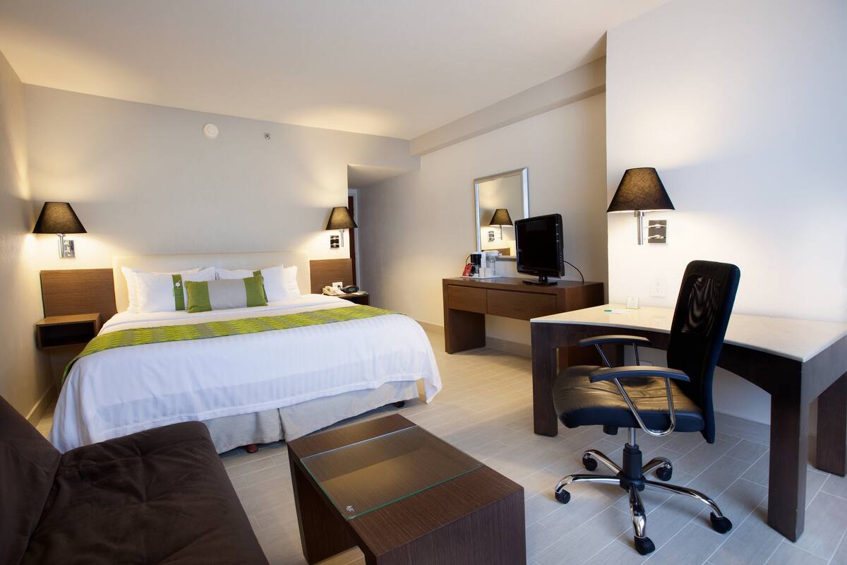 A hotel room with a bed, a desk, a chair, a small table, and two bedside lamps.