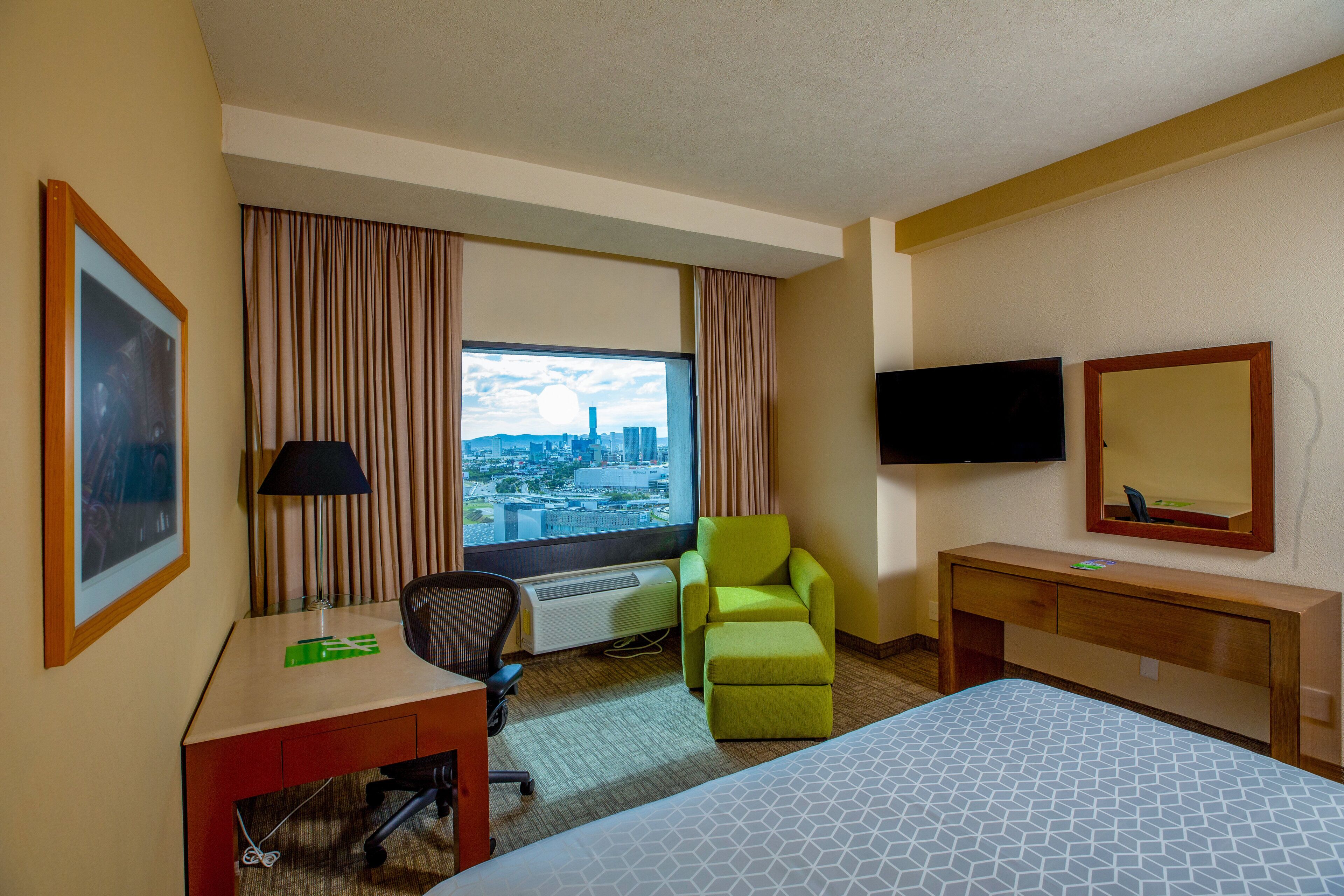 A hotel room with a bed, desk, chair, television, and a window with curtains.