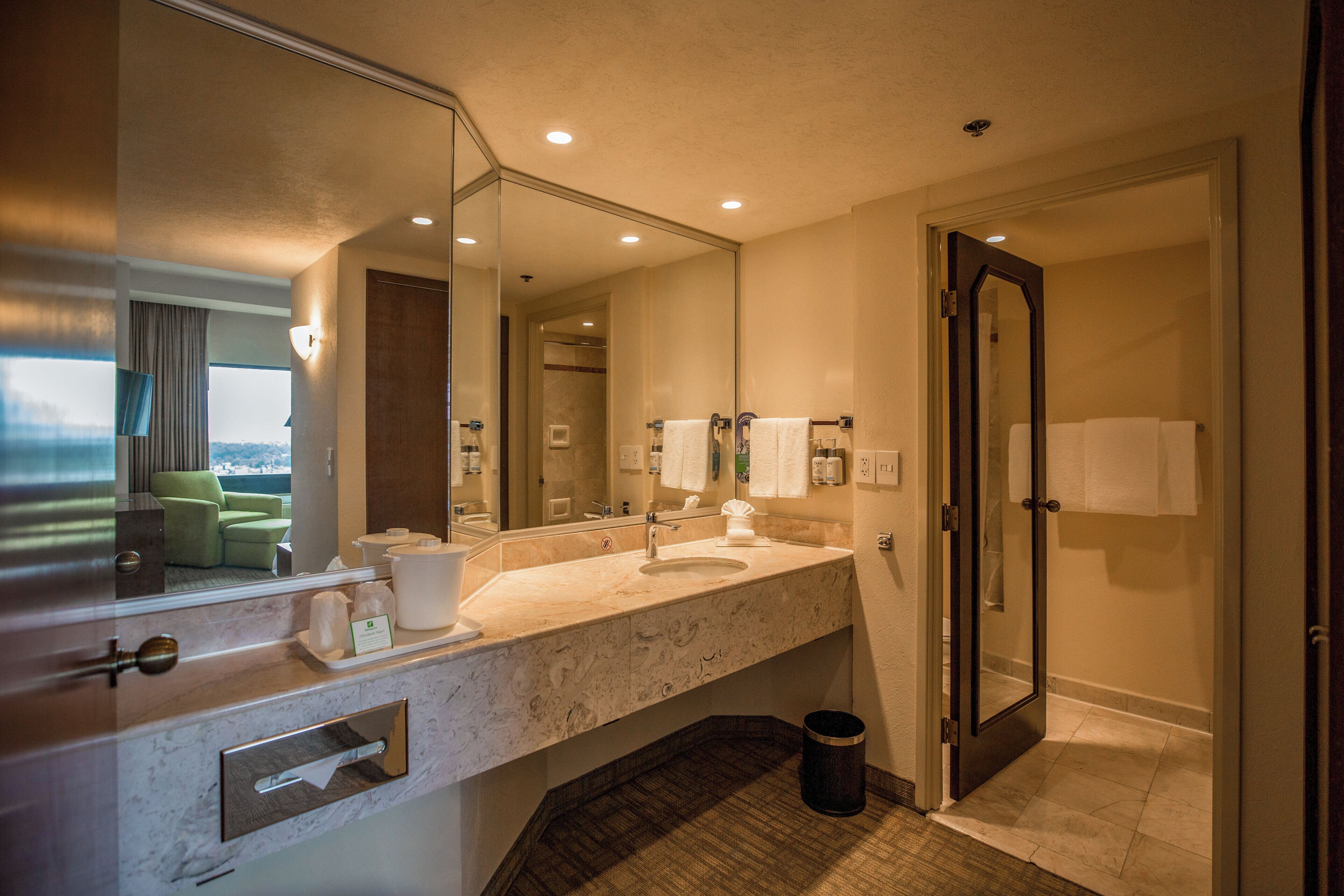 A hotel bathroom with a marble sink, a large mirror, a towel rack, and a trash bin.