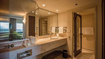 A hotel bathroom with a marble sink, a large mirror, a towel rack, and a trash bin.