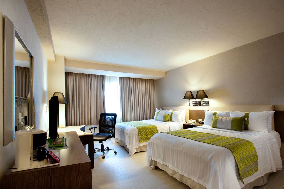 A hotel room with two beds, a desk, a chair, a desk lamp, and a telephone.
