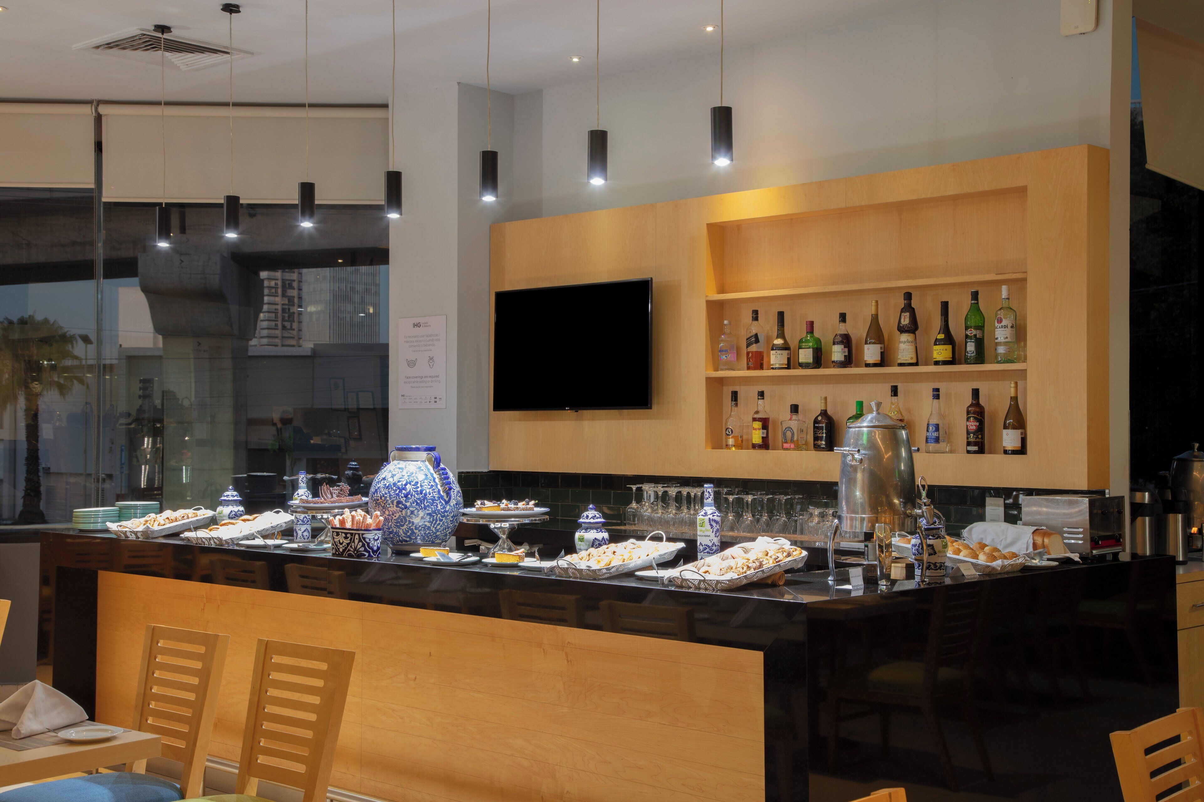 Een moderne bar met een houten toonbank, diverse flessen en een flatscreen televisie.