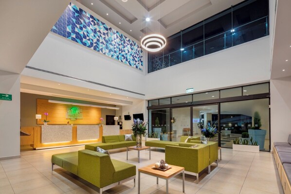 A modern lobby with green seating, a reception desk, and a geometric wall design. - Holiday Inn Puebla La Noria by IHG (Puebla)