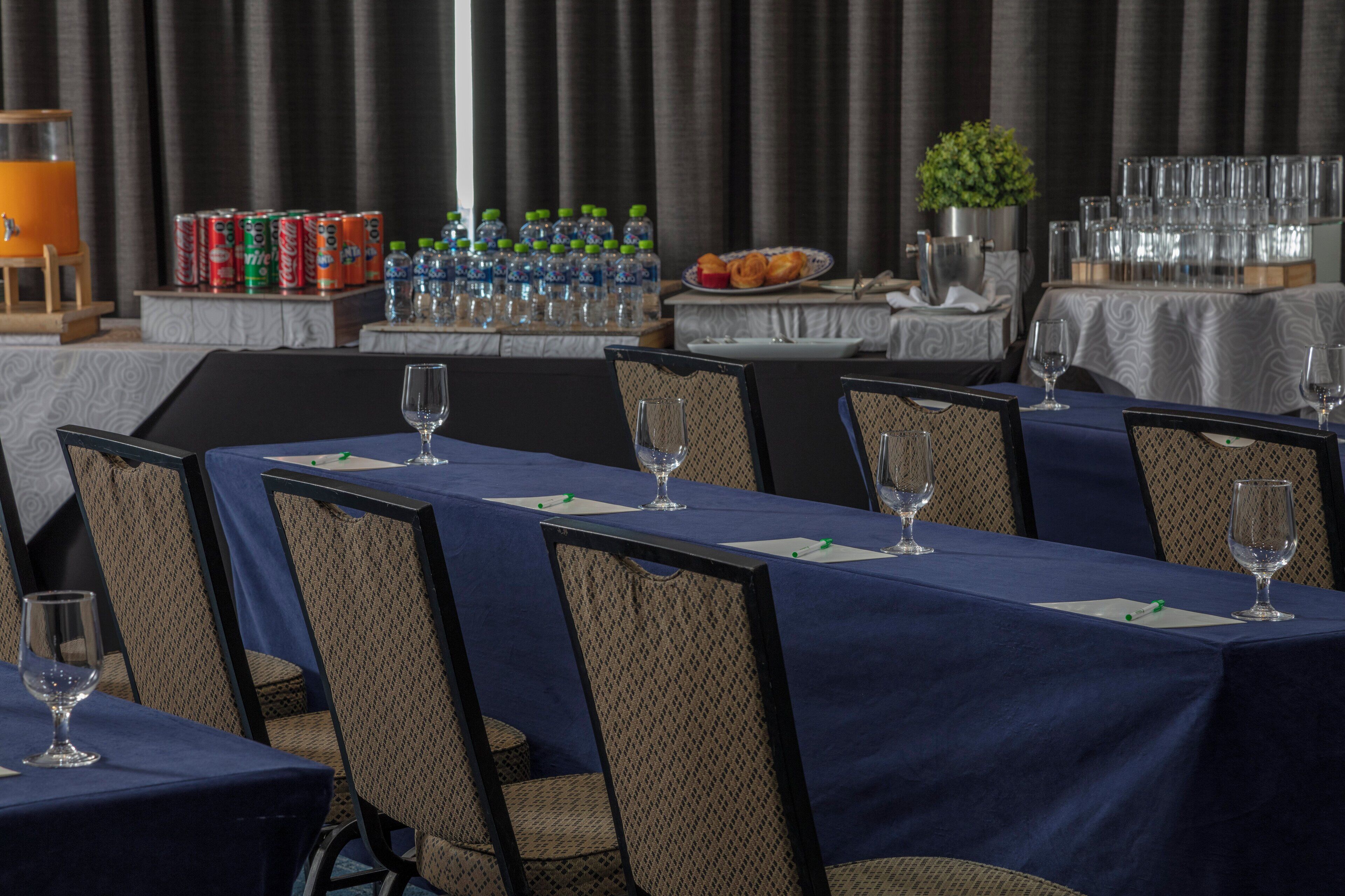 Un salón de conferencias con mesas dispuestas para una reunión, equipado con sillas y copas de vino.