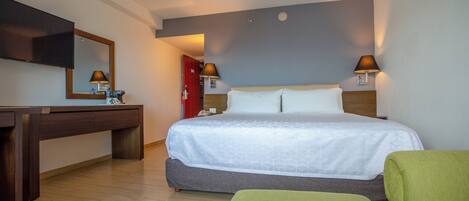 Una habitación de hotel con cama, mesitas de noche, escritorio, silla y televisor.