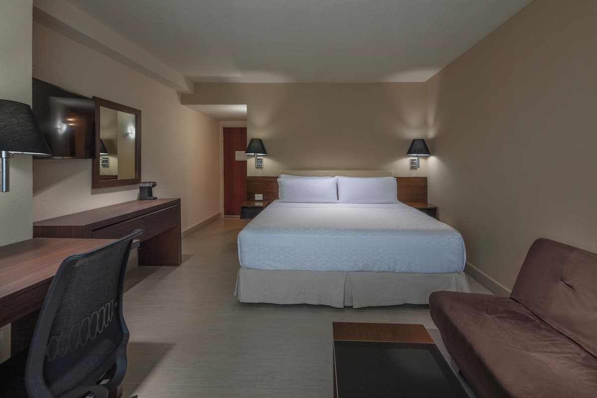 A hotel room with a bed, desk, chair, and a couch.