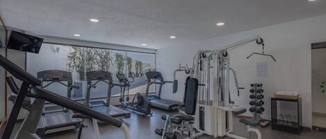 Un gimnasio con cintas de correr, elípticas y equipo para levantamiento de pesas.