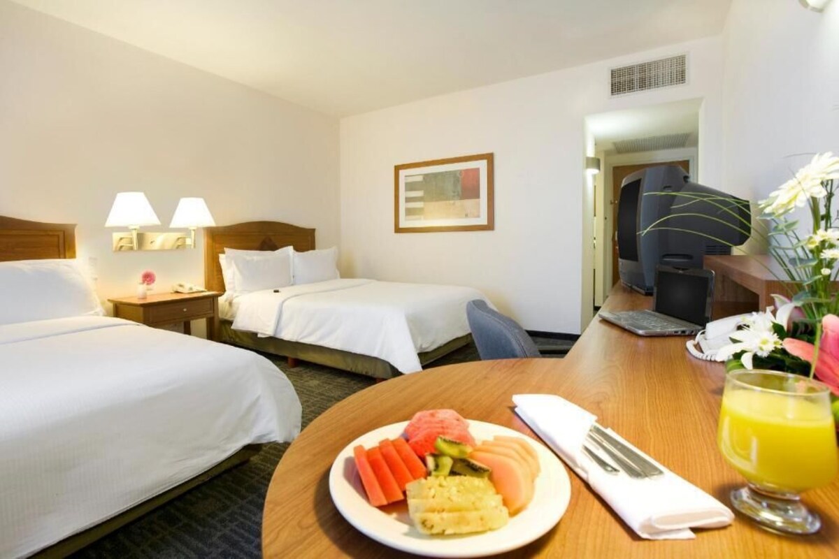 A hotel room with two beds, a desk with a laptop, a plate of fruit, and a glass of juice.