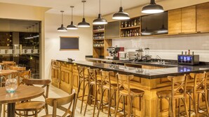 A modern kitchen with wooden cabinets, a central island with bar stools, pendant lighting, and a visible coffee machine.