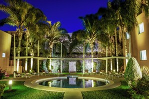 A pool area with lounge chairs and palm trees, surrounded by a building with a green wall and a staircase. -  Fiesta Inn Express San Luis Potosí Oriente (San Luis Potosi)