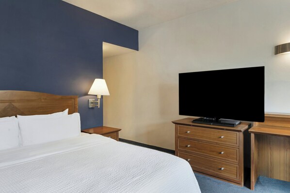 Habitación de hotel con una cama, un televisor sobre una cómoda de madera, una mesita de noche con una lámpara y un televisor fijado a la pared.