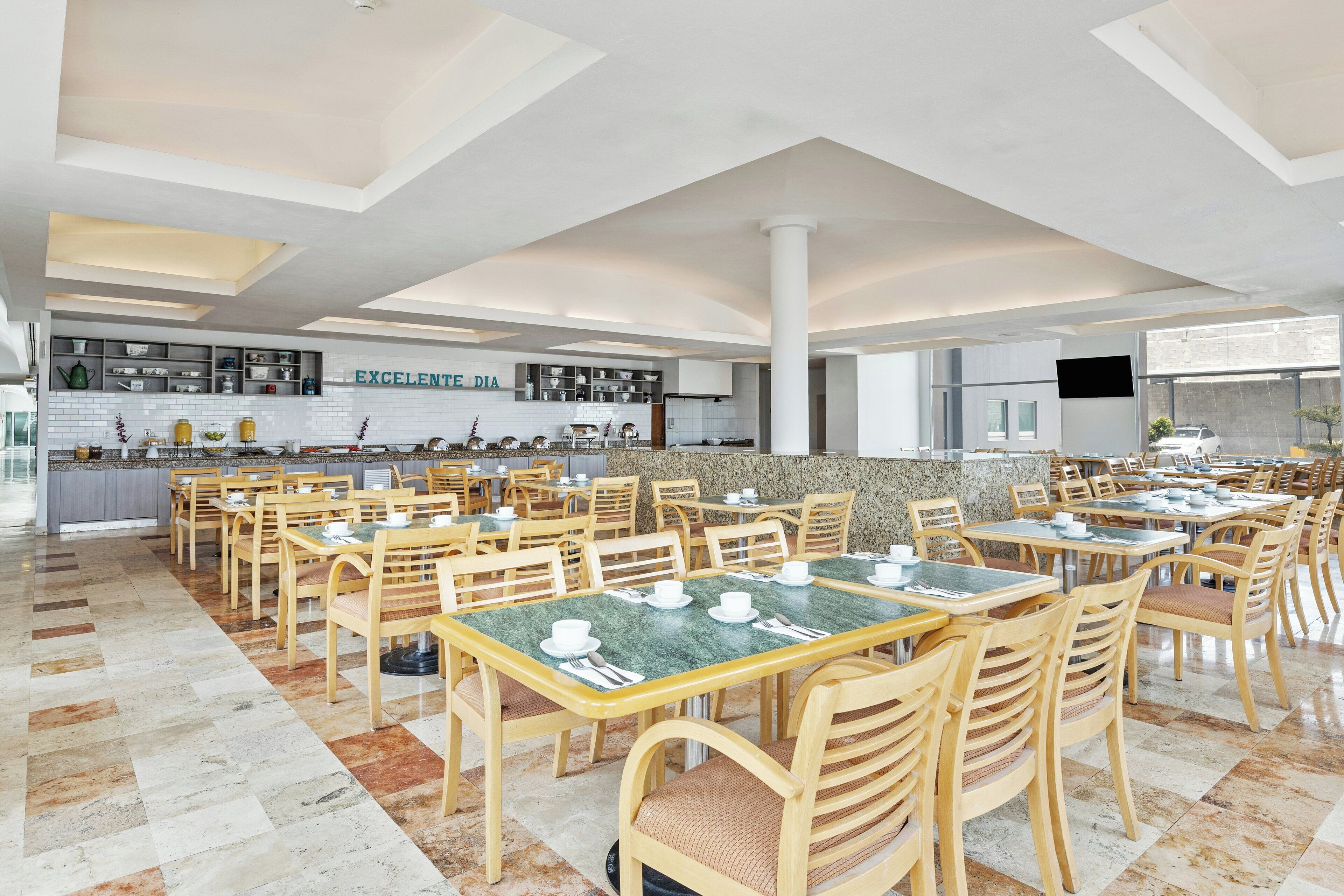 Un comedor espacioso con varias mesas y sillas, una zona de cocina al fondo y un pilar grande en el centro.