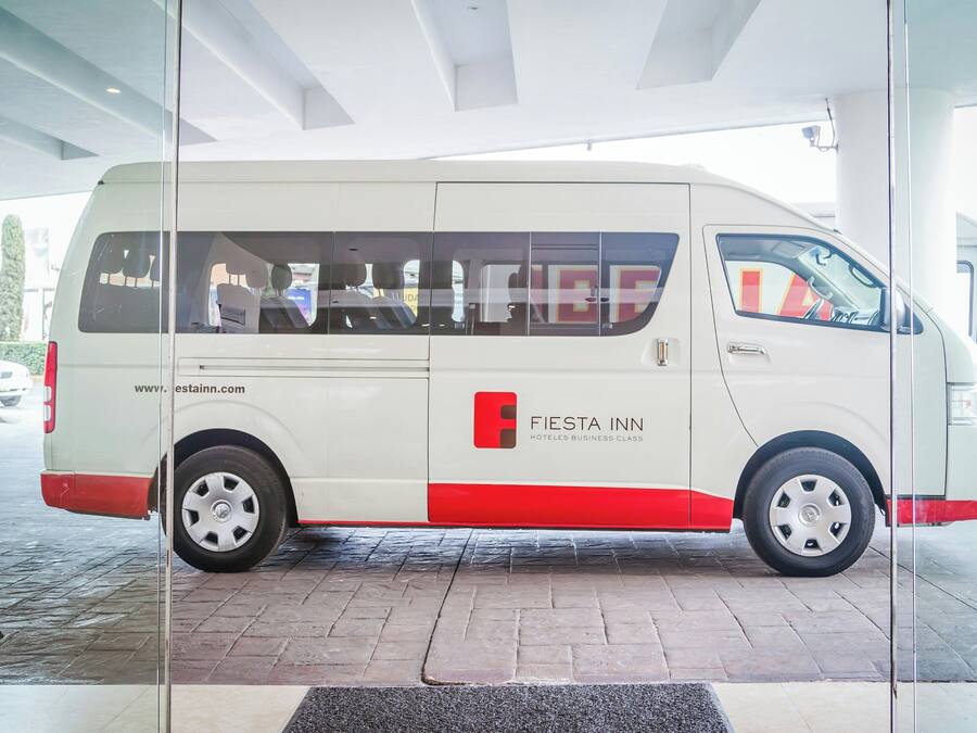 Uma van branca e vermelha com a marca 'Fiesta Inn', estacionada em uma área coberta com piso de azulejos.