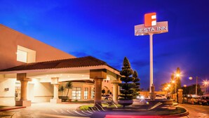 A hotel entrance with a sign reading 'FIESTA INN,' a fountain, and a parking lot. - Fiesta Inn Saltillo (Saltillo)