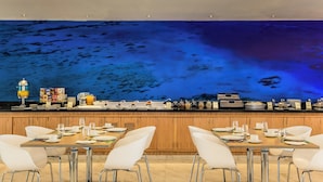 A breakfast bar with a blue ocean-themed wall, wooden cabinets, and white chairs. - Fiesta Inn Saltillo (Saltillo)