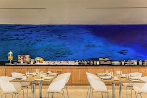 Una barra de desayuno con un revestimiento de pared azul con temática marina, armarios de madera y sillas blancas.