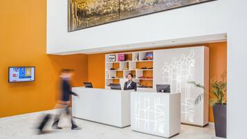 A modern reception desk with a white and grey design, a large painting on the wall, and a potted plant on the right.