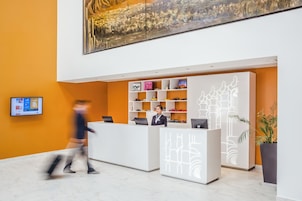 Un mostrador de recepción moderno con diseño blanco y gris, un cuadro grande en la pared y una planta en maceta a la derecha.