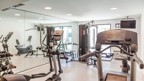 A gym with various exercise machines, a mirrored wall, and a television mounted on the wall. - Fiesta Inn Saltillo (Saltillo)